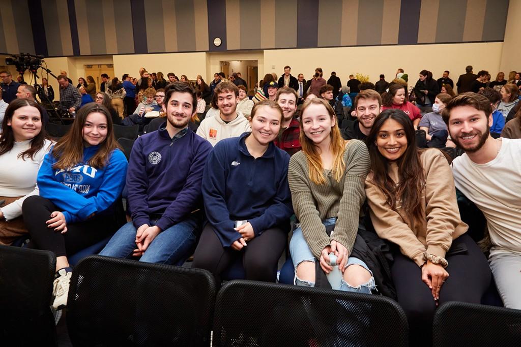 A group of U N E students sit in a row of the audience at a President's Forum