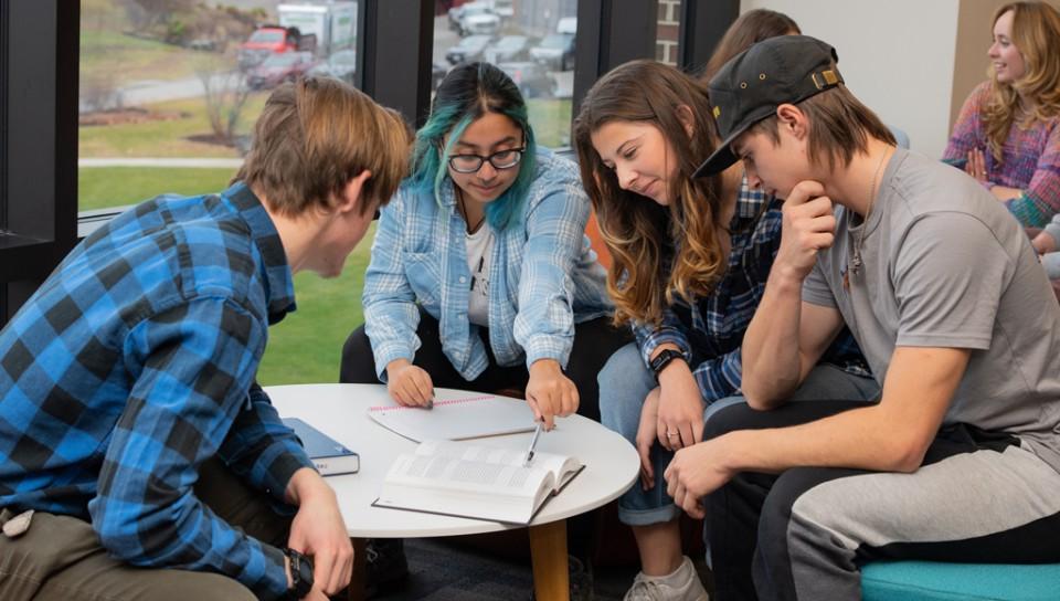 A group of students sit over a table and study in the Commons