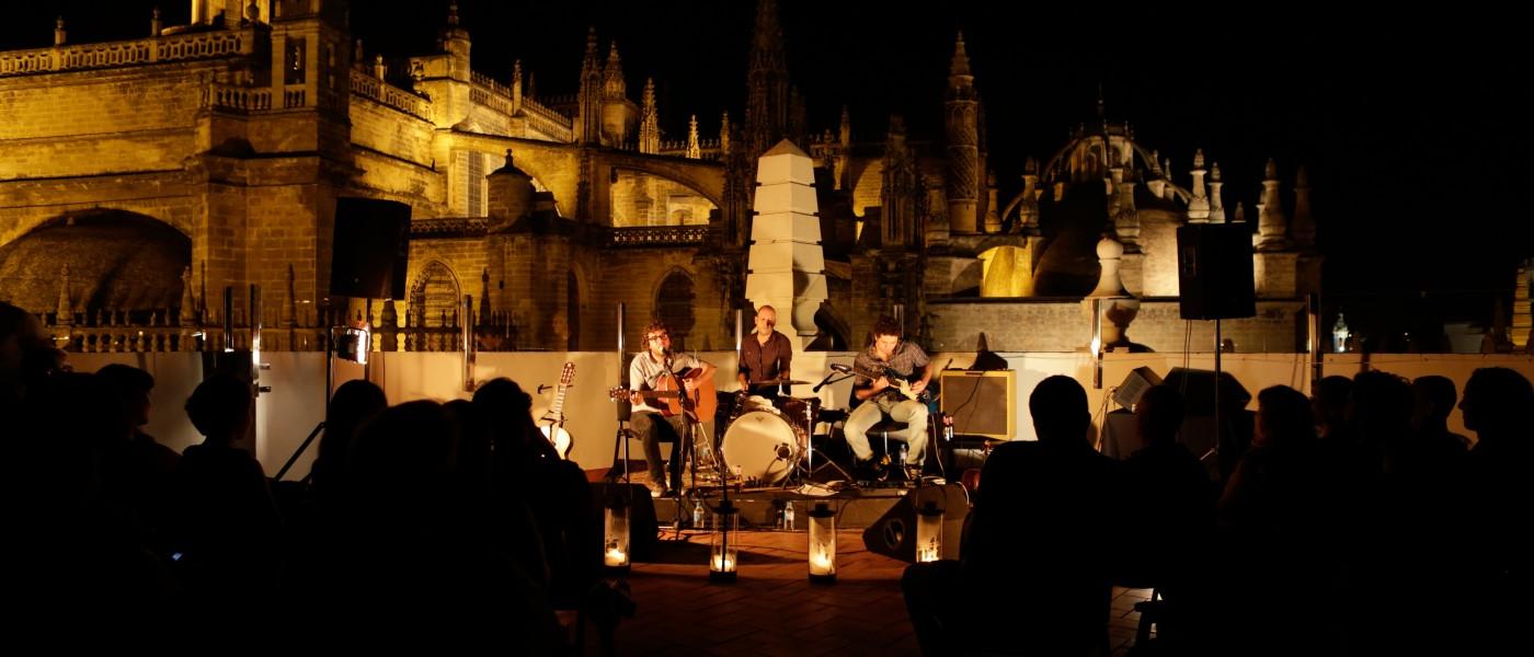 People listen to an evening musical performance at an outdoor plaza in Seville