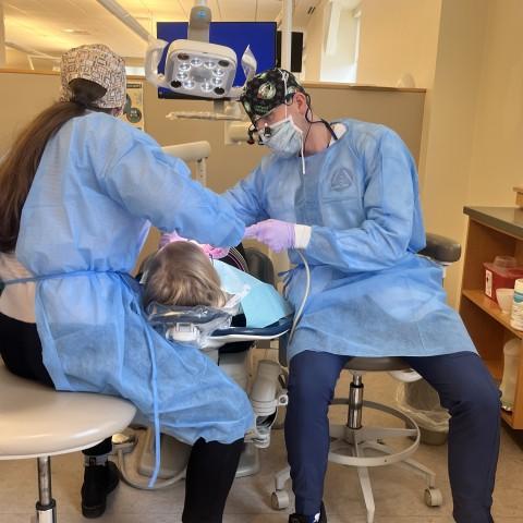 Two dental students clean a patient's teeth in the oral health clinic